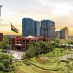 Aerial view of Gujarat International Finance Tech City with modern skyscrapers against a sunset sky, lush green landscape, and an Indian flag. Text reads "Click here to read more."